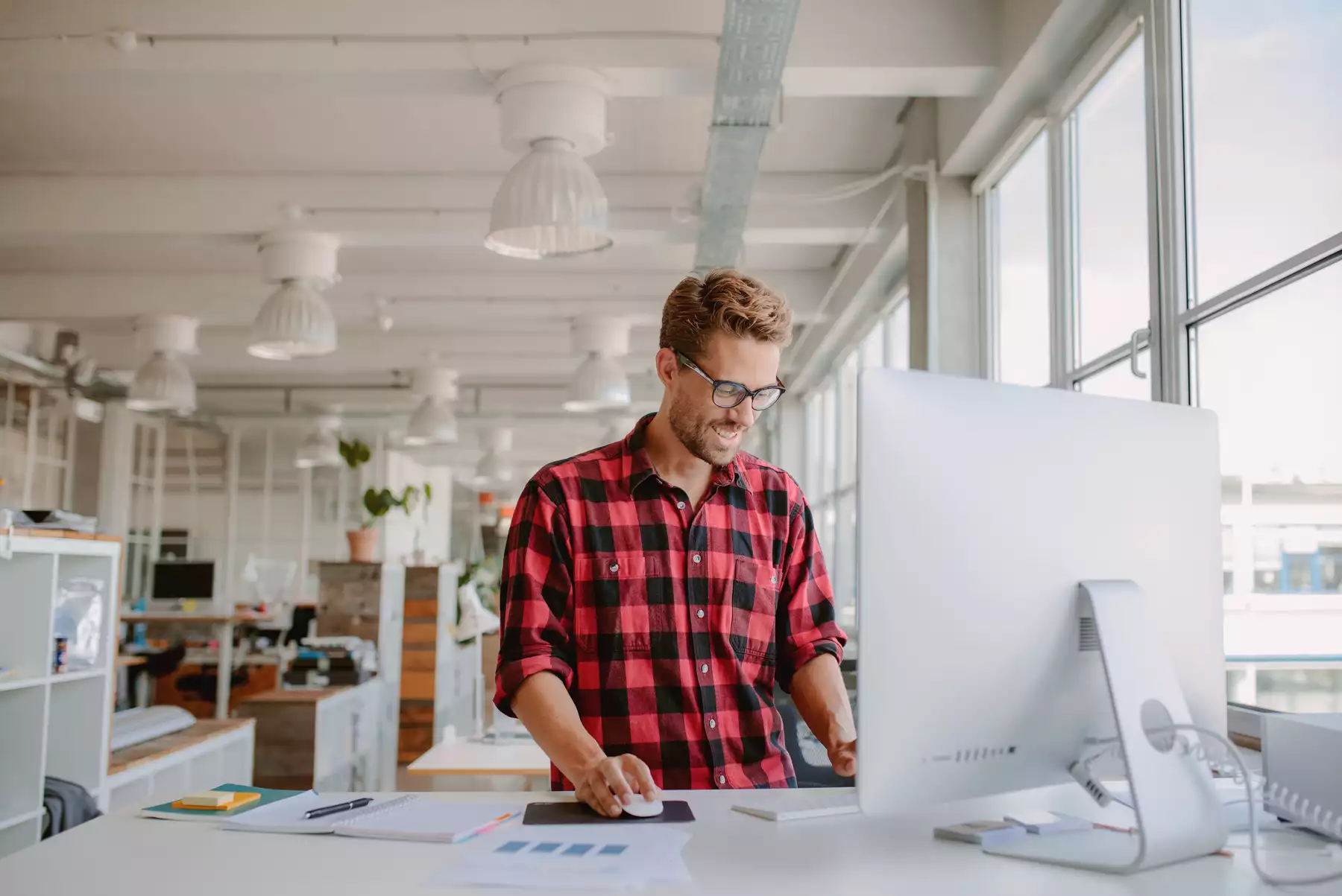 Shot of happy young man working on desktop computer in modern workplace