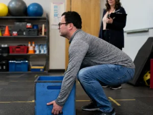 Candidate performing a physical ability test by lifting a weighted box under supervision during a pre-employment physical abilities testing assessment in a controlled evaluation environment.
