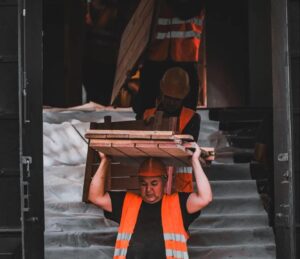 Man carrying a heavy load in a workplace setting, illustrating physical strain and early risk factors associated with musculoskeletal disorders and workplace injury prevention efforts.