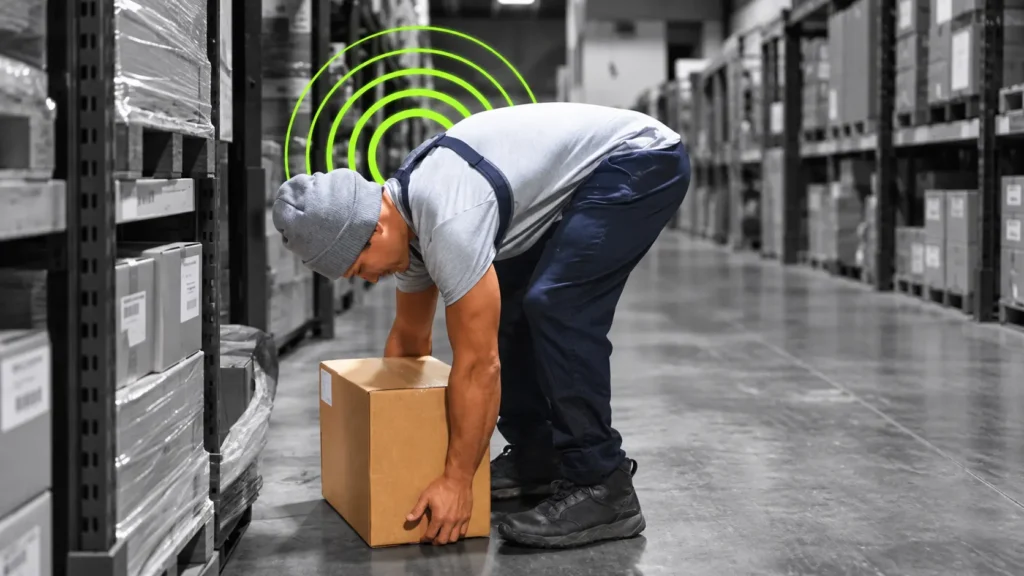 Worker lifting a box in a warehouse using ergonomic lifting techniques to reduce workplace injury risk